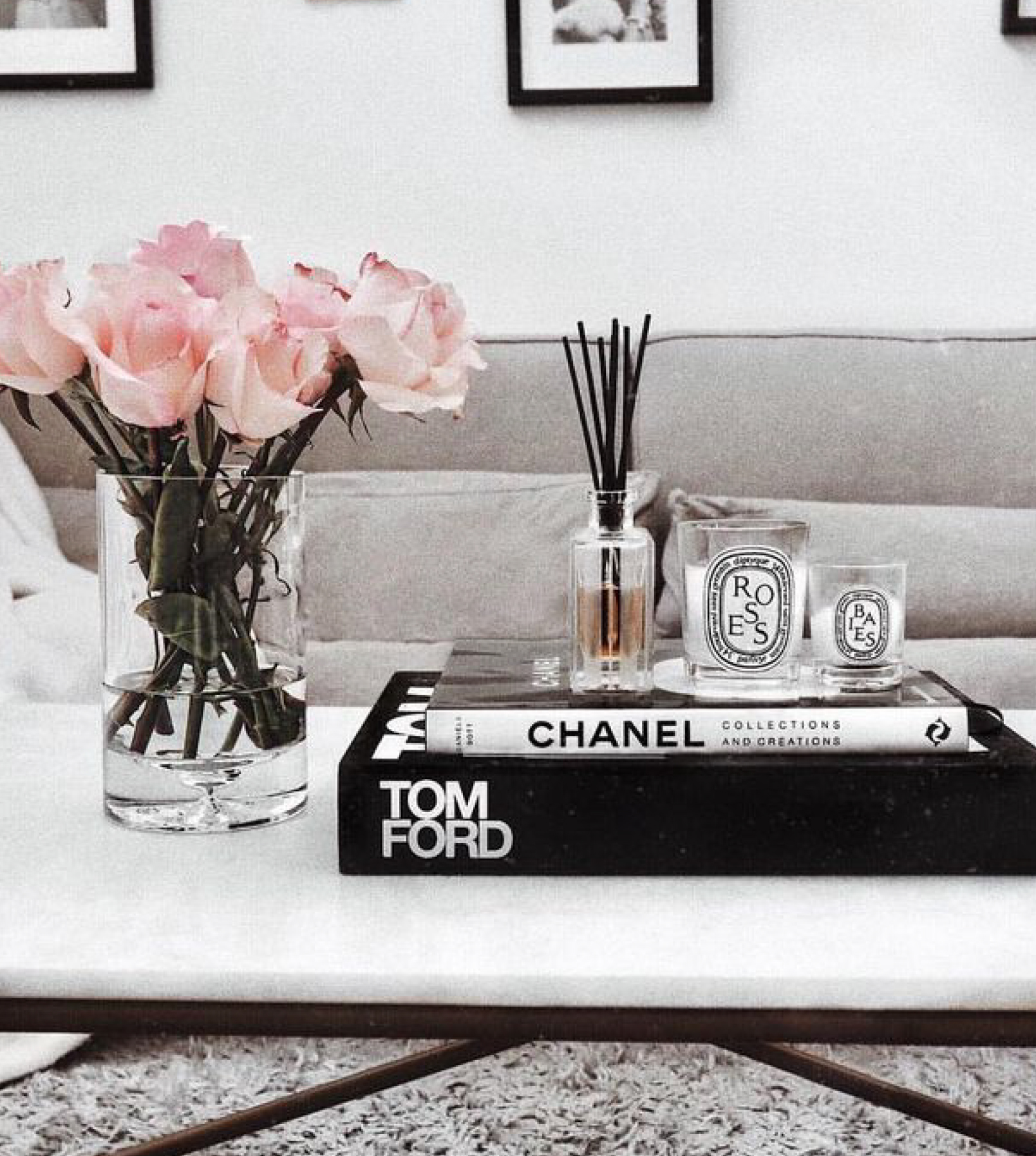 White marble coffee table complete with premium scented candles and incense resting on Tom Ford and Chanel coffee table books, beside vase of pink roses.